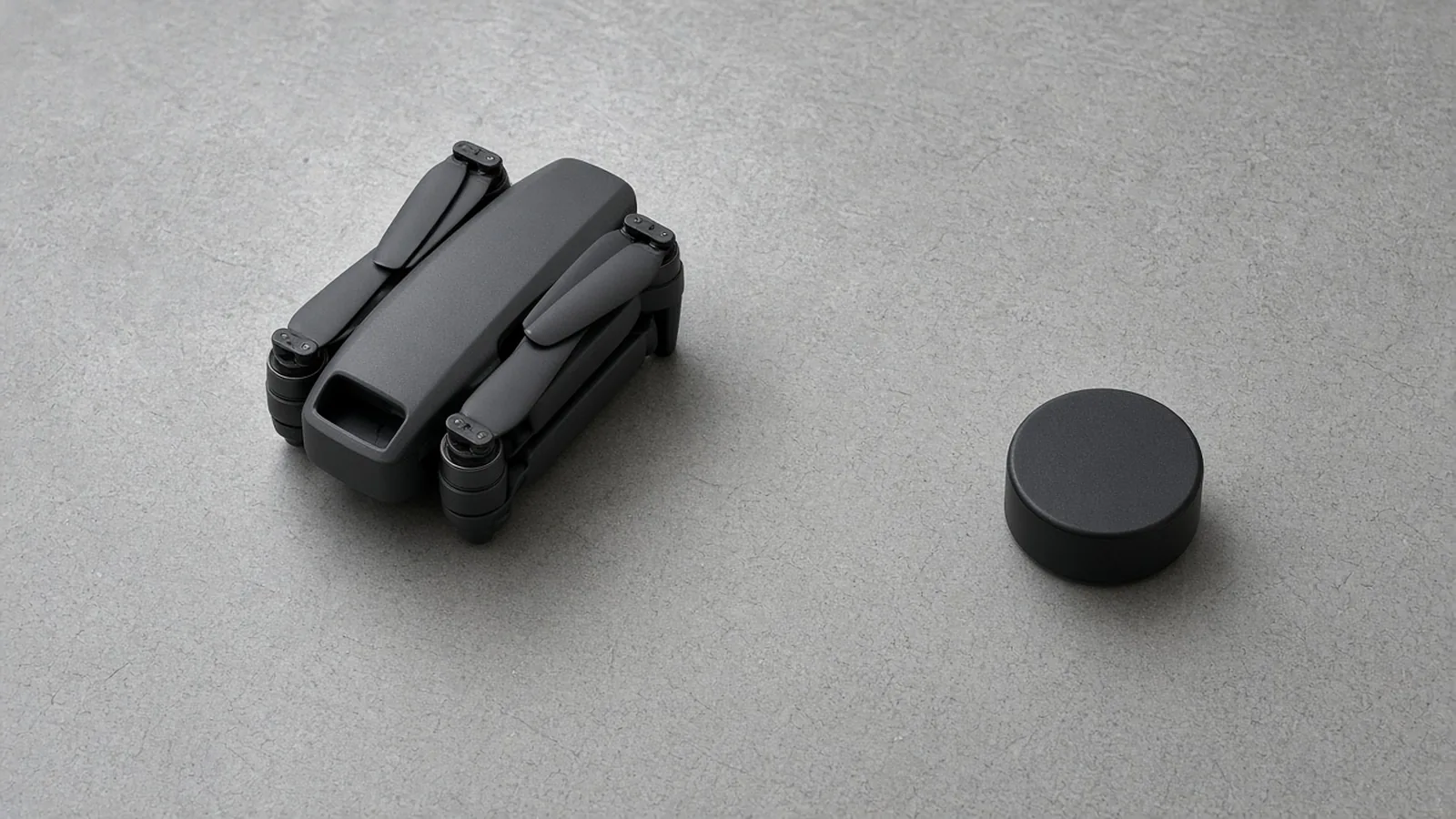A folded quadcopter and a separate black module on a gray table